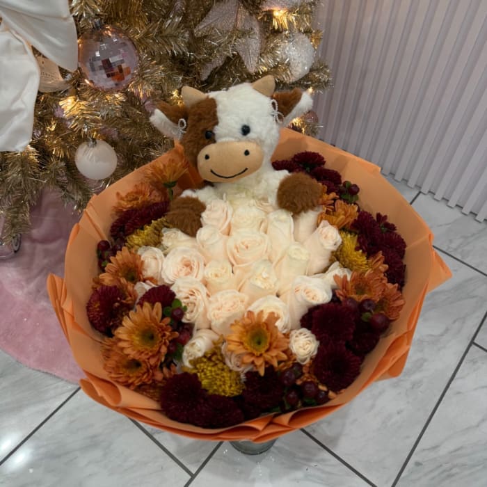 Bouquet of cream roses and orange chrysanthemums with a plush cow topper