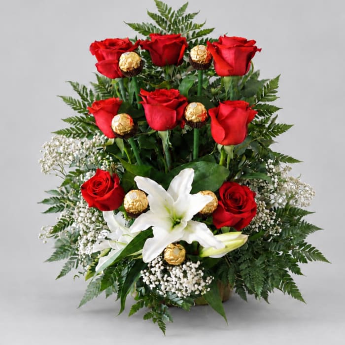 Red roses and white lilies arranged with gold-wrapped chocolates in a vase