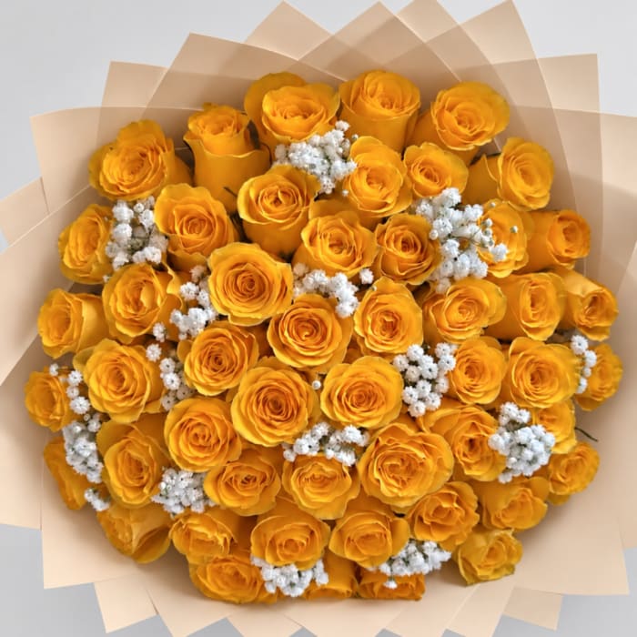 Bouquet of yellow roses with small white filler flowers wrapped in beige paper