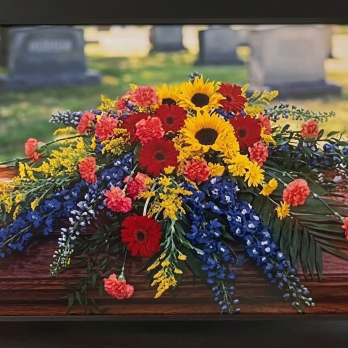 Colorful floral casket spray with sunflowers, red gerberas, and blue flowers