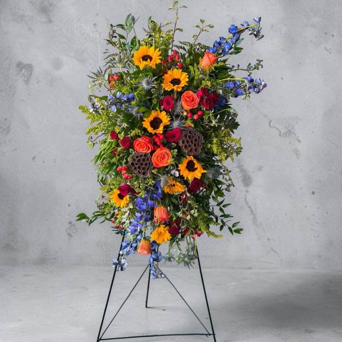 Tall standing floral spray with sunflowers, roses, and blue flowers on a metal easel