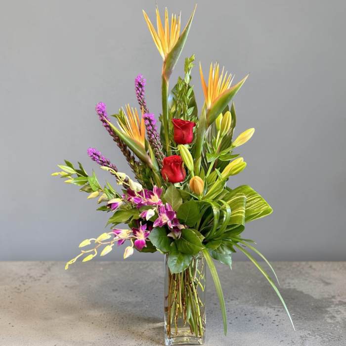 Tropical bouquet with red roses and orchids in a clear glass vase