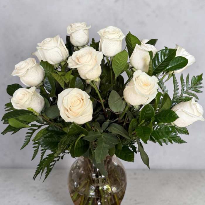 White roses arranged in a glass vase with dark green foliage