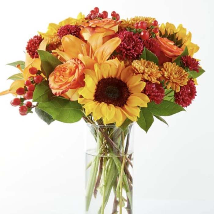 Bouquet of sunflowers, roses, and mums in a clear glass vase
