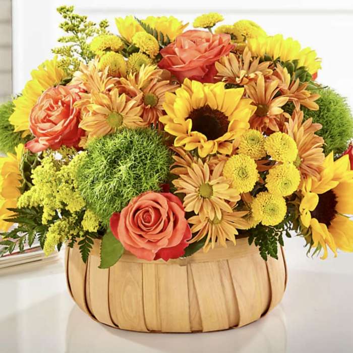 Basket arrangement of yellow sunflowers, coral roses, and orange daisies