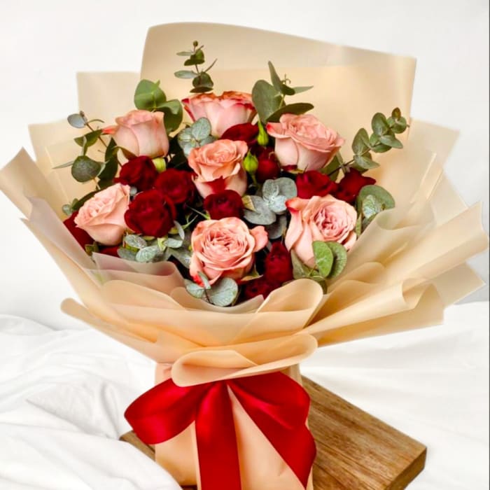 Bouquet of pink and red roses wrapped in beige paper with a red ribbon