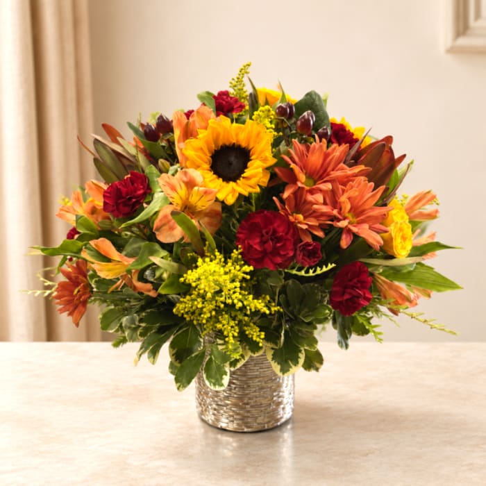 Mixed bouquet with sunflowers, orange blooms, and red flowers in a woven vase