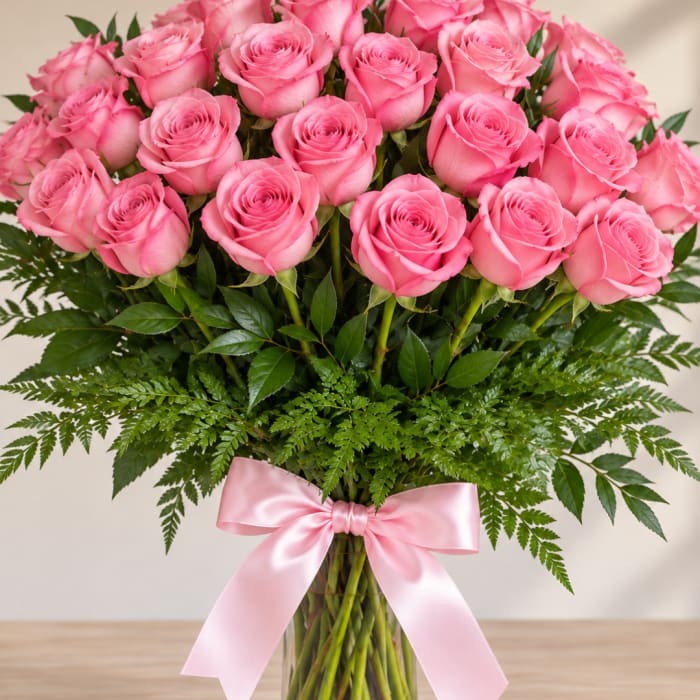 Pink roses arranged in a clear glass vase with a pink ribbon bow