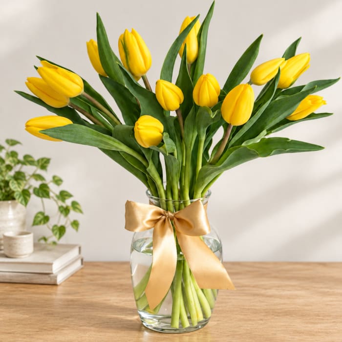 Yellow tulips in a clear glass vase with a gold ribbon
