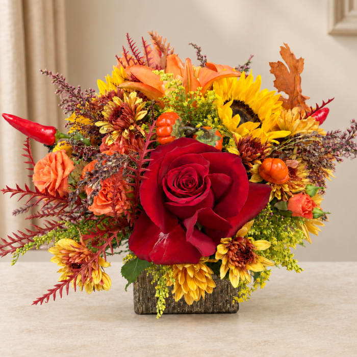 Autumn bouquet with a red rose, sunflowers, and orange blooms in a square vase