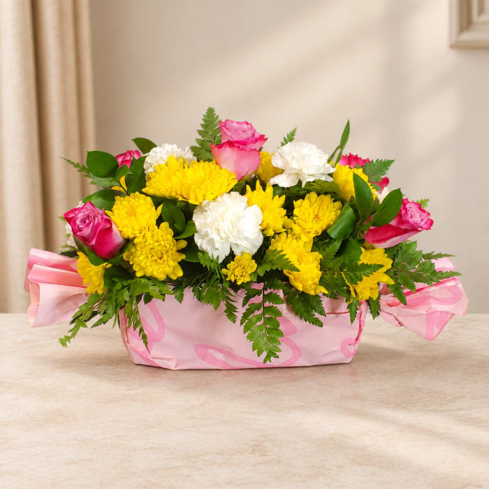 Pink roses and yellow chrysanthemums in a pink wrapped basket