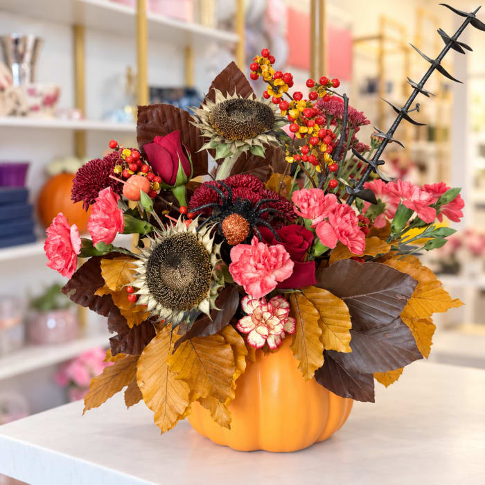 Fall floral arrangement in an orange pumpkin container with sunflowers and pink blooms