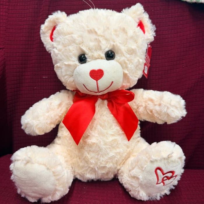 Cream teddy bear with a red bow sitting on a burgundy chair