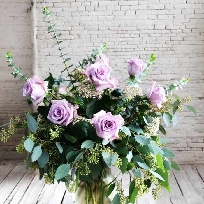 Lavender roses arranged in a glass vase with mixed greenery