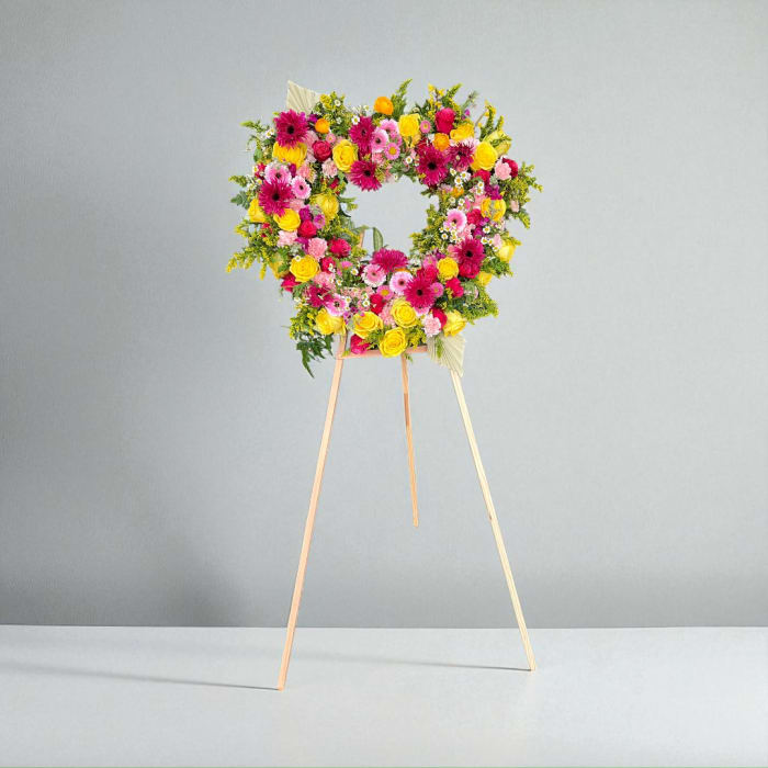Heart-shaped floral standing wreath on a wooden easel with pink, yellow, and orange blooms