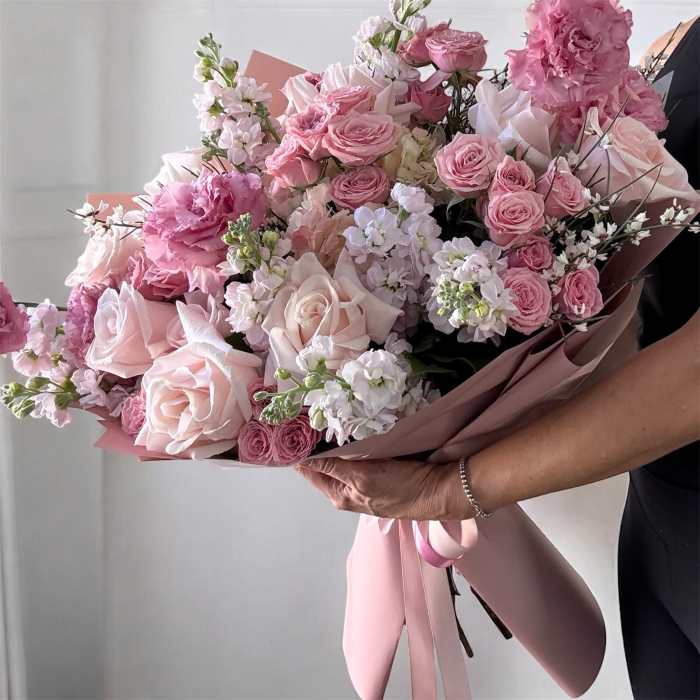 Large pink bouquet of roses and ruffled blooms wrapped in blush paper