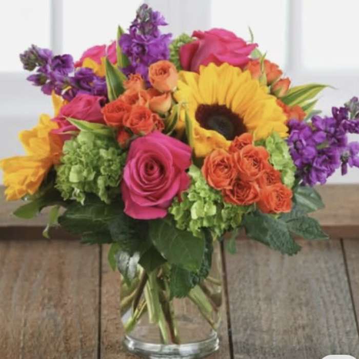 Colorful bouquet of roses, sunflowers, and purple flowers in a glass vase