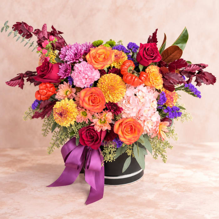 Mixed bouquet of roses, chrysanthemums, and hydrangeas in a black hat box with purple ribbon