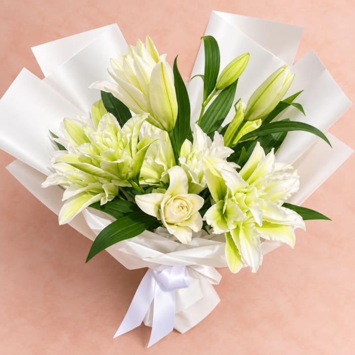 Bouquet of white lilies and a cream rose wrapped in white paper