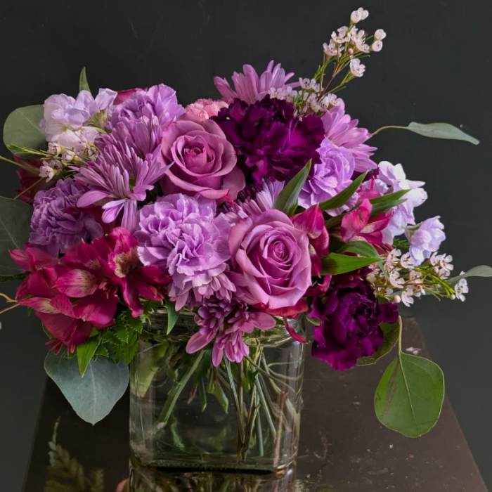 Lavender and magenta roses, carnations, and mixed blooms in a clear glass cube vase