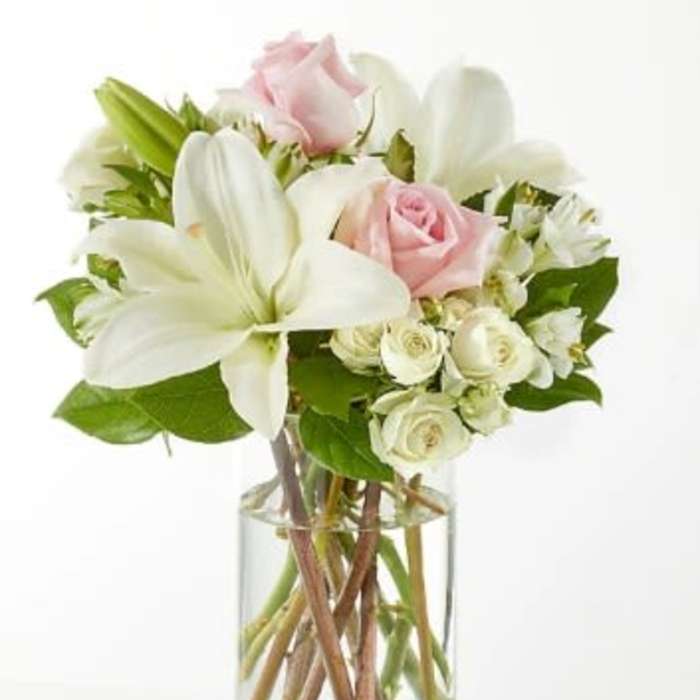 Clear glass vase with white lilies and pale pink and white roses.