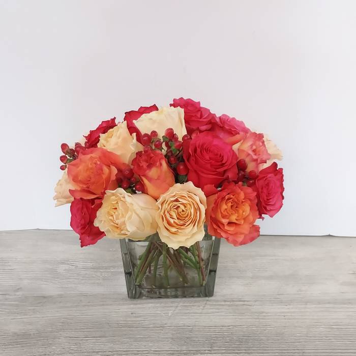Low arrangement of red and peach roses with red berries in a clear glass cube vase