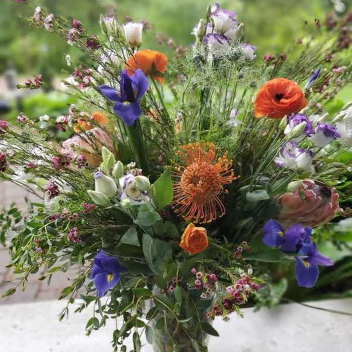 Mixed bouquet of orange, purple, and white flowers in a clear glass vase
