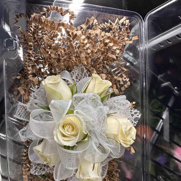 White rose corsage with silver mesh ribbon in a clear plastic box with brown paper fill