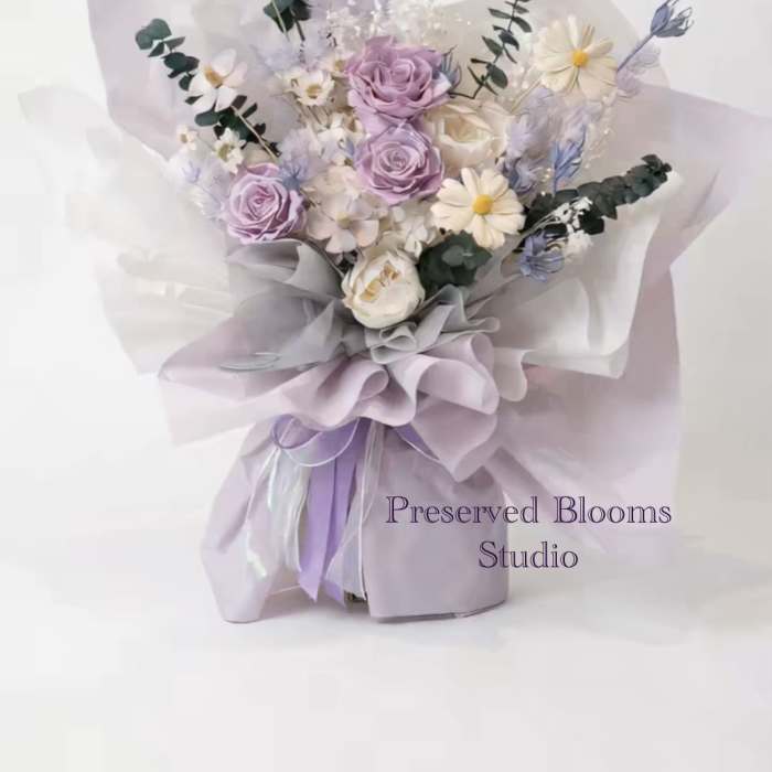 Hand-tied bouquet of lavender roses and white daisies wrapped in layered lilac and white paper.