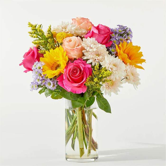 Mixed bouquet of roses, sunflowers, and daisies in a clear glass vase