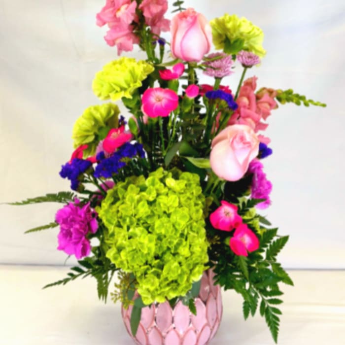 Tall mixed arrangement of pink and green flowers in a pink textured vase