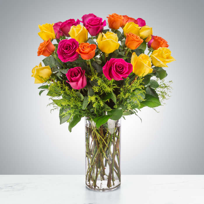 Tall arrangement of hot pink, yellow, and orange roses in a clear glass cylinder vase