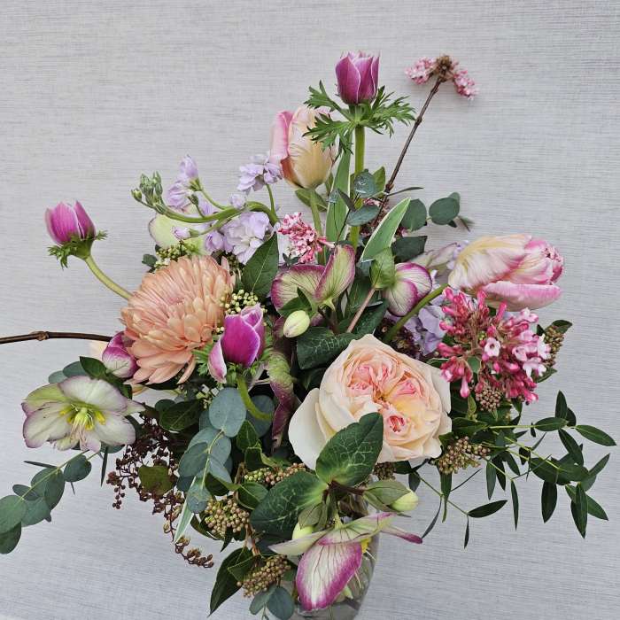 Loose arrangement of pink and peach blooms, including roses and tulips, in a clear glass vase