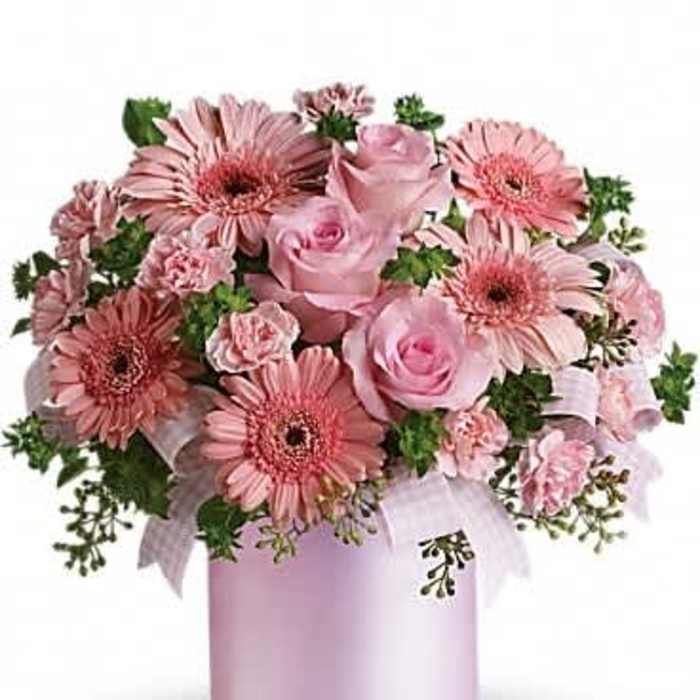 Pink arrangement of gerbera daisies, roses, and carnations in a pale pink cylinder container with ribbon
