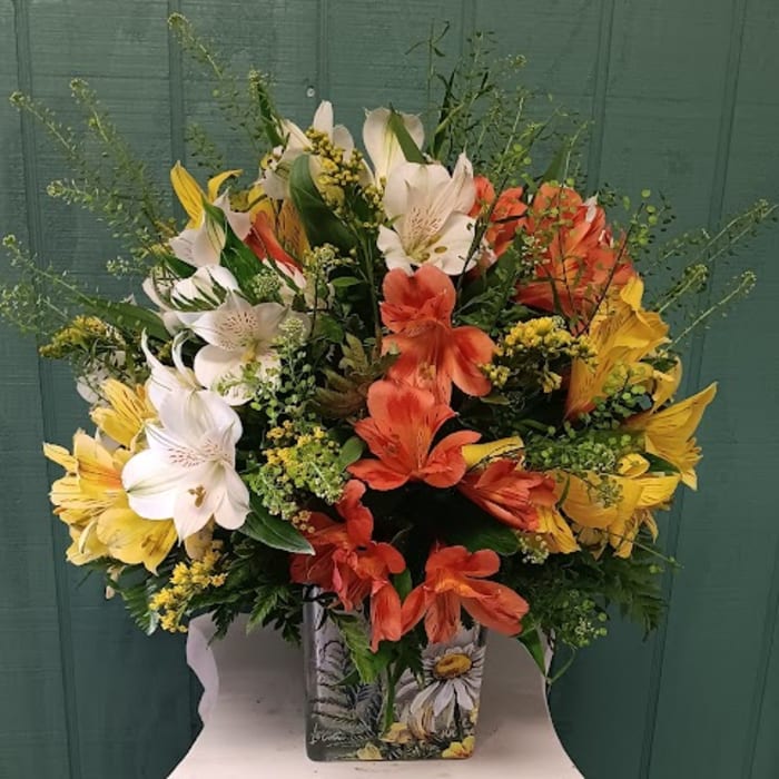 Mixed bouquet of white, yellow, and orange lilies in a decorative vase