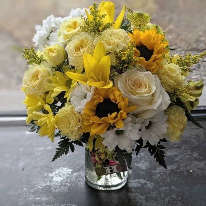Yellow and white bouquet with sunflowers, lilies, roses, carnations, and daisies in a clear glass vase