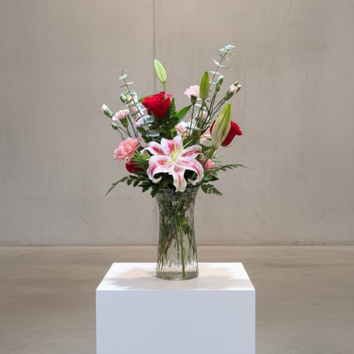 Mixed bouquet with lilies and red roses in a clear glass vase