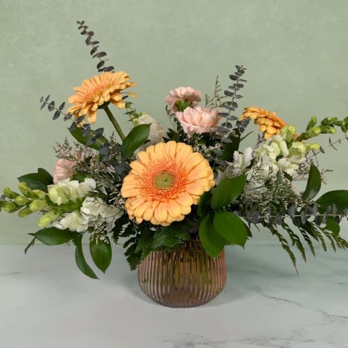 Peach gerbera daisies and pale pink carnations in a ribbed glass vase
