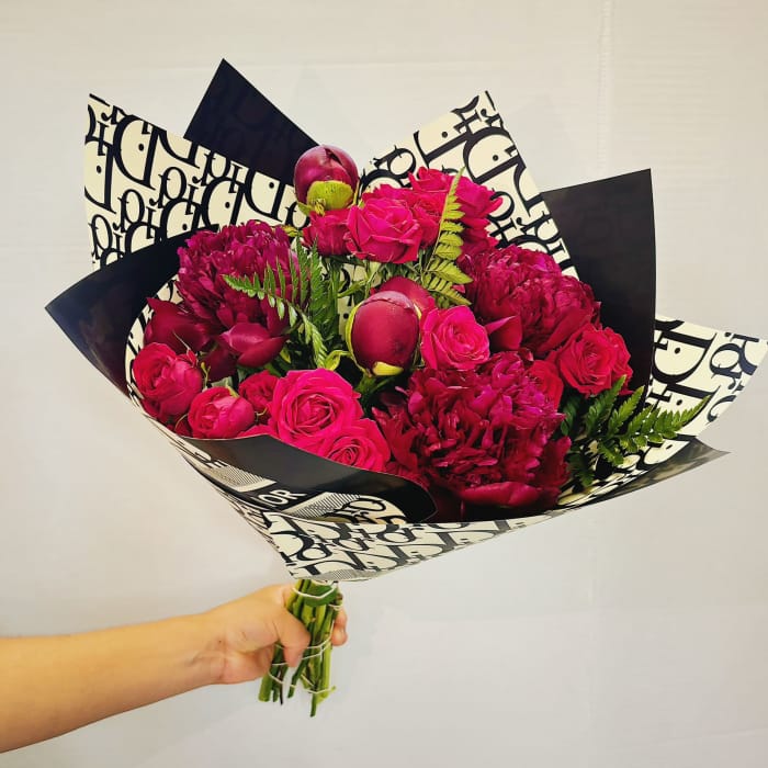 Handheld bouquet of hot pink roses and deep magenta blooms in patterned wrap