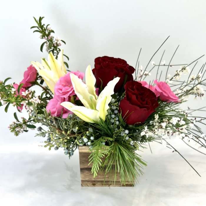 Arrangement of red and pink roses with white lilies in a wooden box