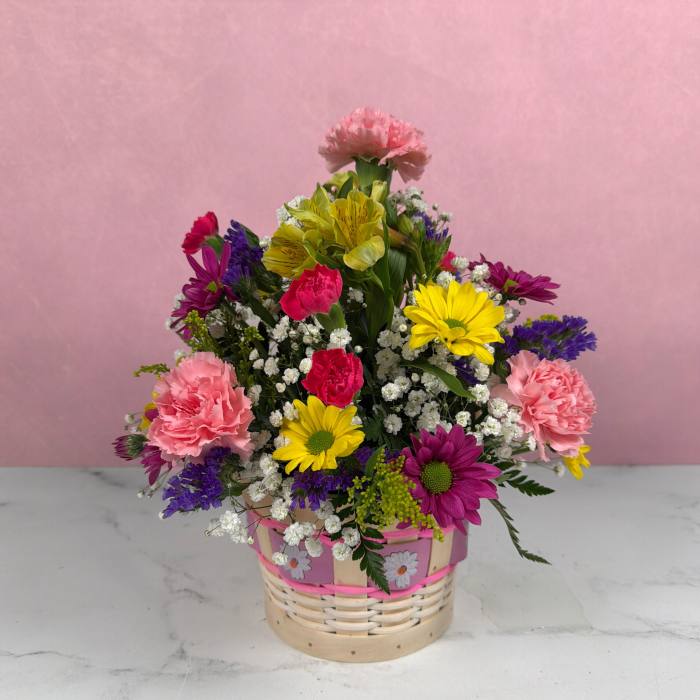 Basket of mixed pink carnations, yellow and purple daisies, and white filler flowers.