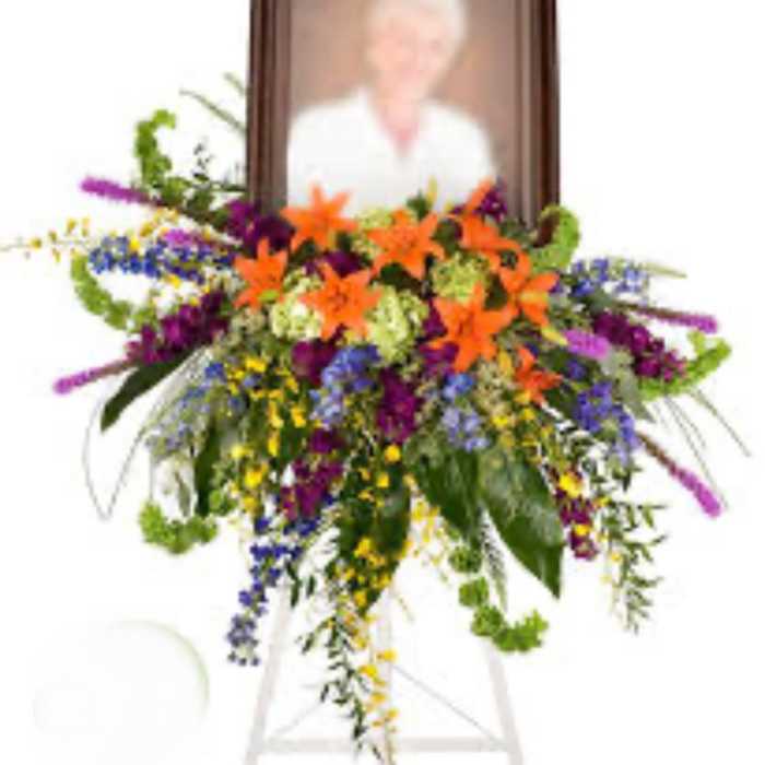 Standing funeral spray with orange lilies and purple flowers around a framed portrait