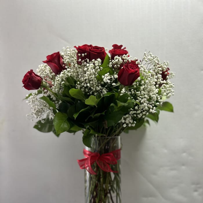 Red roses and baby's breath in a clear glass vase with a red ribbon
