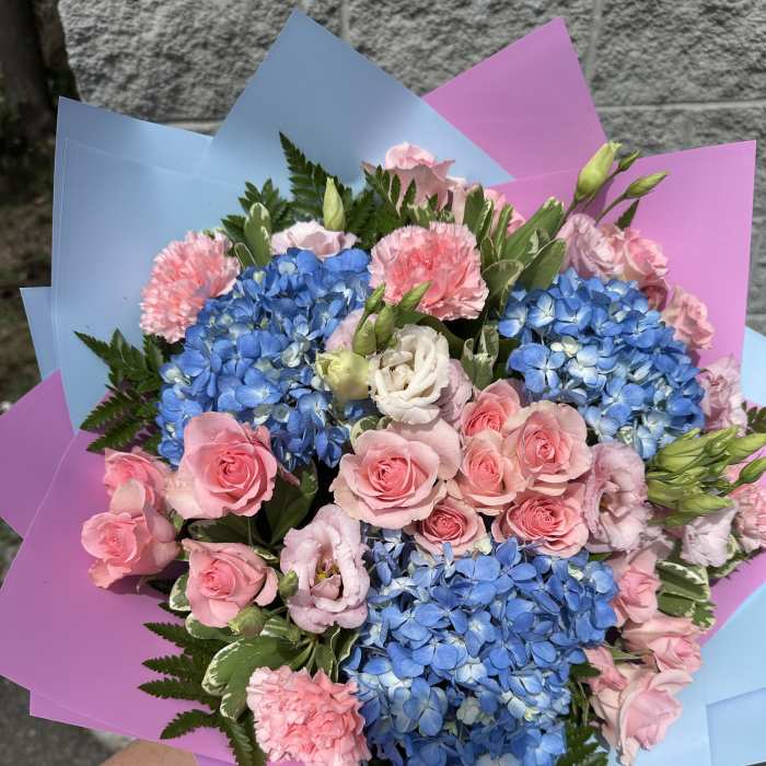 Bouquet of blue hydrangeas, pink roses, and carnations wrapped in pastel paper