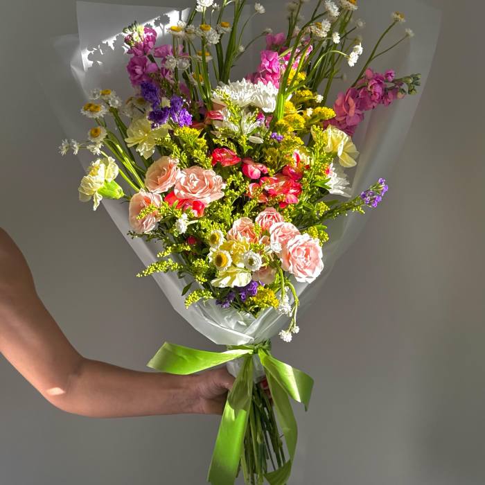 Handheld bouquet of pink, yellow, white, and purple flowers wrapped in clear paper