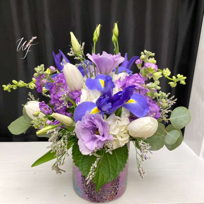 Purple and white floral arrangement in a mosaic glass vase