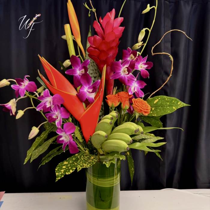 Tropical flower arrangement in a tall glass vase with orchids and orange blooms
