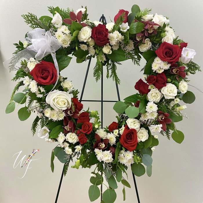 Heart-shaped floral wreath with red and white roses on a black stand