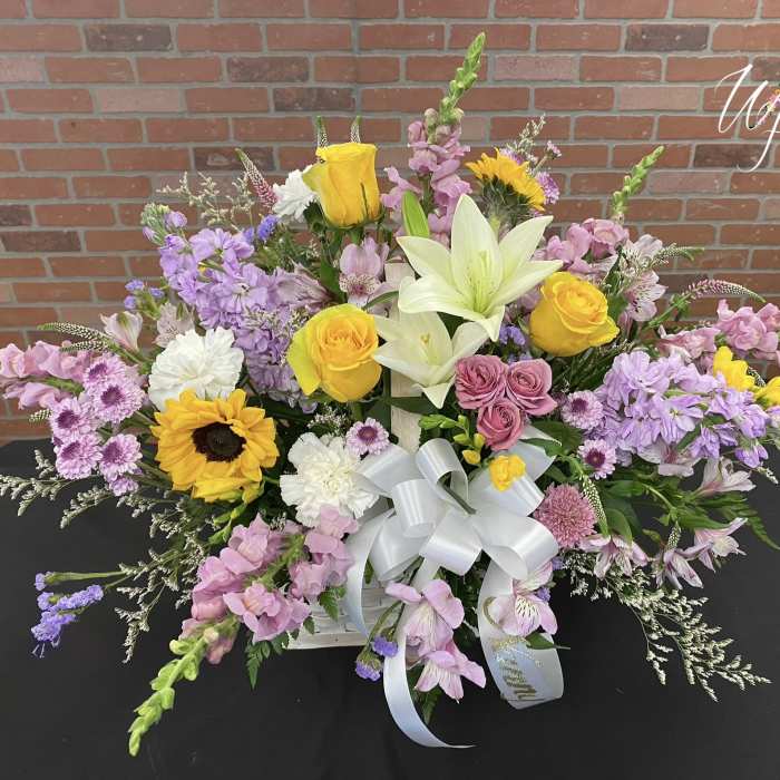 Mixed floral arrangement with yellow roses, lilies, sunflowers, and pink blooms in a white basket
