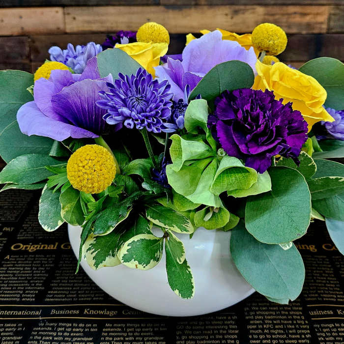 Purple and yellow floral arrangement in a white bowl vase